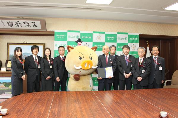 まるいのと市長を真ん中にしてその両隣にスーツを着た男女が並んでいる写真